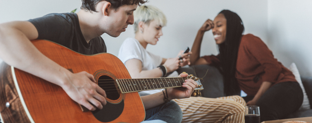 Roommates sharing a living space, with one playing an acoustic guitar.