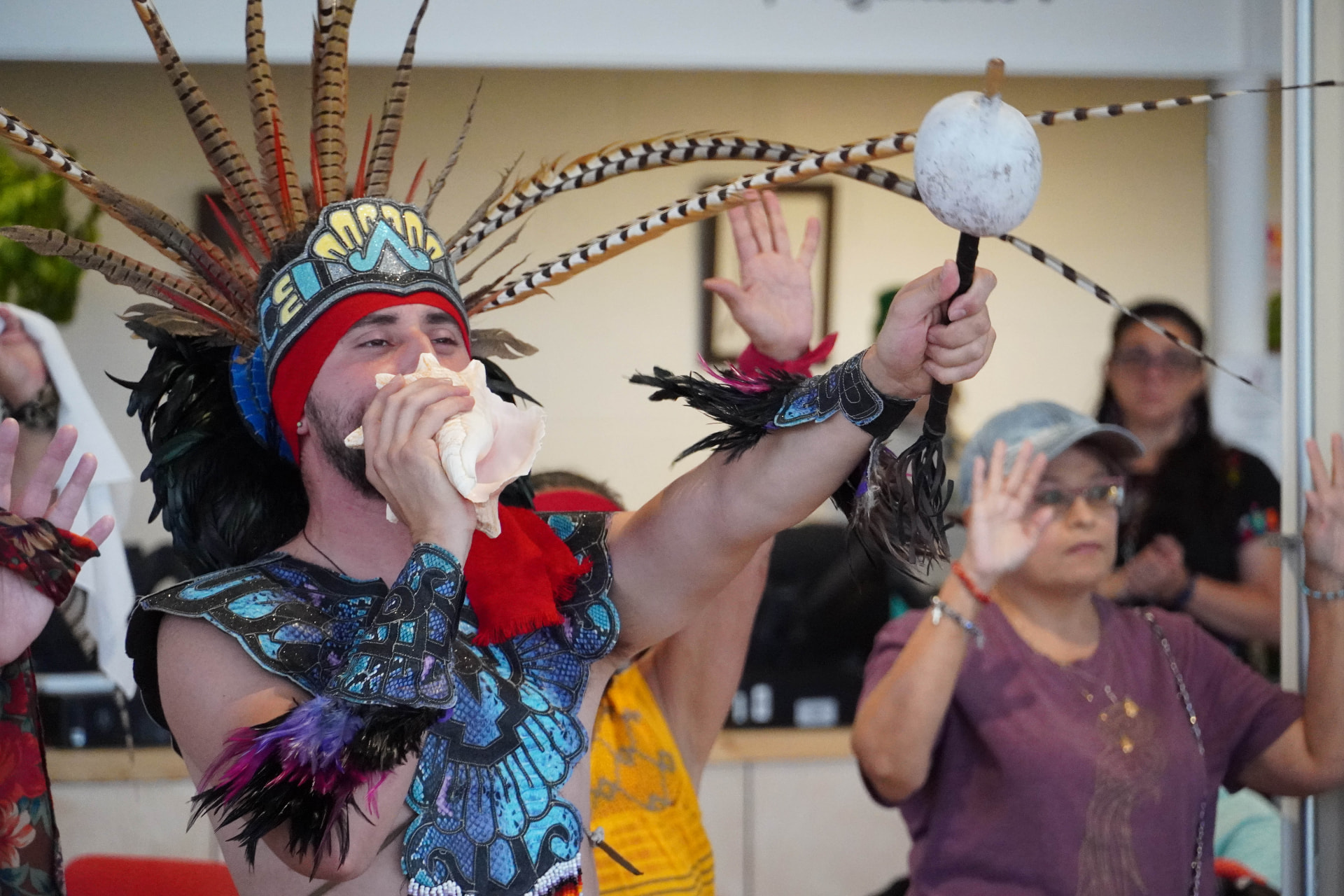 A performer in a feathered headdress sounding a conch shell horn at a LOUD series event