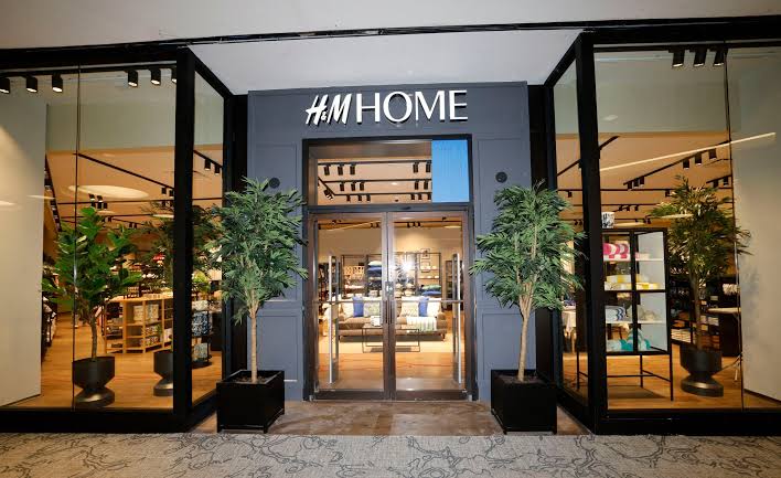 H&M Home storefront with its glass entrance framed by two potted trees